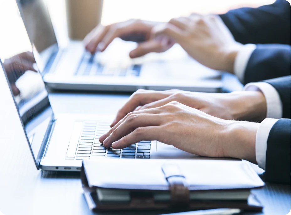 スーツ姿のビジネスパーソンがノートPCで作業している手元の写真